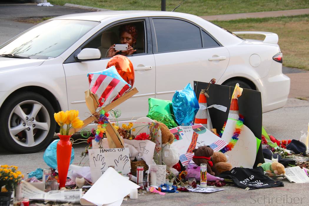 A women drives by flowers and placards in Ferguson, MO, Monday, August 25, 2014, in what constitutes one of the three installations in memorial of Michael Brown, killed earlier this month. This memorial is located in the middle of Canfield drive, on the spot he has been shot at by officer Darren Wilson, promoting days of unrest in the St Louis suburb. (Yann Schreiber)